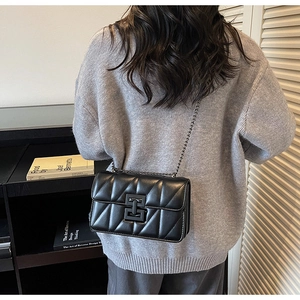 Detail of a black quilted leather crossbody bag with a metal chain strap and lock