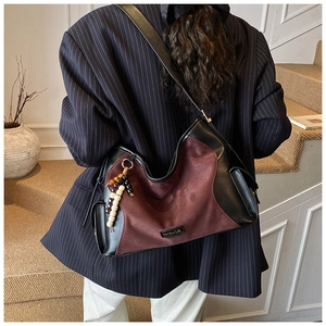 Detail of burgundy suede and black leather stitching with a wood bead tassel on the bag
