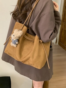 Brown suede tote bag with plush bear charm shown from a side view on a female model