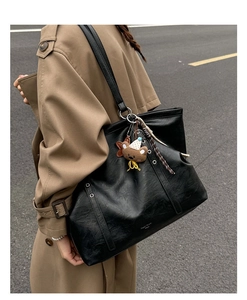 Detail of black pebbled leather tote bag with silver grommet and plush bear charm accent