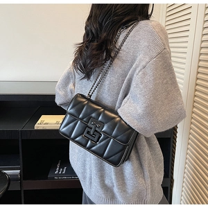 Detail of black quilted crossbody bag with matte metal chain strap on model's shoulder