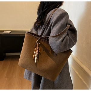 Detail view of large brown suede tote bag with wooden bead pendant and slim shoulder straps