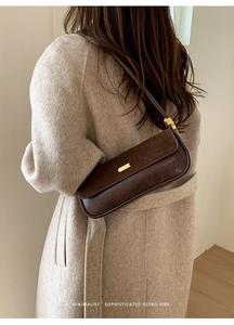 Detail view of dark coffee leather baguette bag with a gold buckle on a beige coat