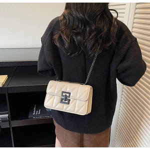 Model wearing a beige quilted chain crossbody bag with unique black metal clasp lock