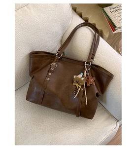 Detail of a dark brown tote bag featuring metallic eyelets and cute bear charm pendant