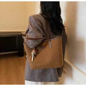 Detail of a brown suede tote bag with colorful bead charm on a grey blazer model