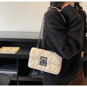 Detail of cream quilted crossbody bag featuring black matte square buckle and chain strap