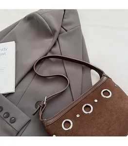 Detailed macro view of dark brown suede shoulder bag with silver eyelet embellishments