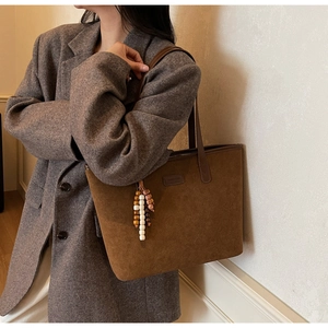 Brown suede tote bag with wooden bead charm worn by a model in a minimal setting