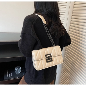 Detailed view of beige quilted crossbody bag with black lock and chain strap on model