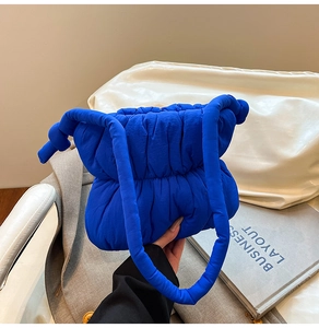 Detailed close-up of bright blue quilted puffer bag featuring stylish knotted handle detail