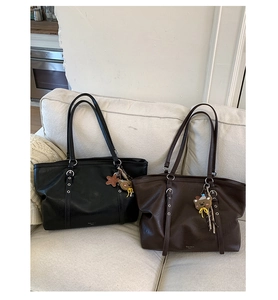 Detail of black and brown tote bags on sofa featuring fine leather texture and charms