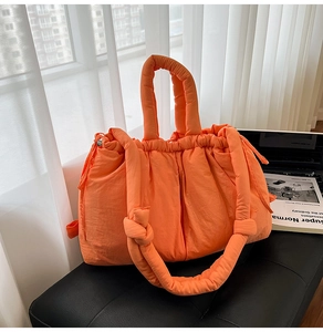 Detail of orange quilted puffer tote bag featuring thick knotted rope handles and drawstring
