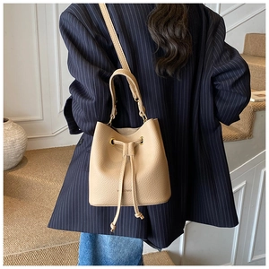 Detailed view of beige bucket bag showing litchi grain texture and gold eyelets