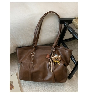 Detail of dark brown leather tote bag with metallic ring decor and cute bear charm accessory