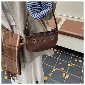 Detailed close-up of dark brown suede shoulder bag with vintage silver eyelets and texture