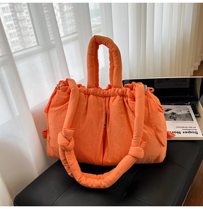 Detail of bright orange padded tote bag with drawstring closure on a black leather bench