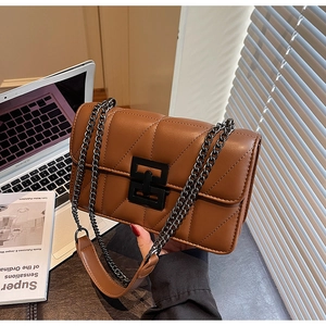 Close-up of brown quilted leather bag with black metal lock and chain strap on a desk