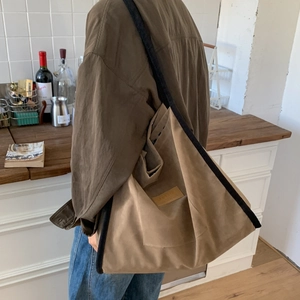 Detail of a khaki canvas tote bag with black strap and leather logo tag on a shoulder