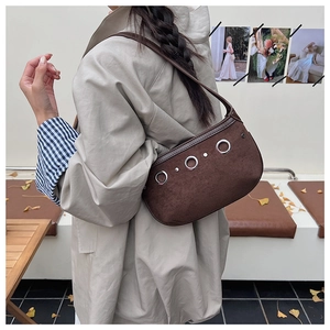 Detail view of brown suede shoulder bag with decorative silver grommets on a model