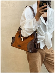 Detail of the suede patchwork tote bag featuring a wooden bead tassel and metal brand logo