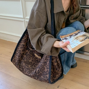 Close-up of a leopard print canvas tote bag with black strap and leather logo patch
