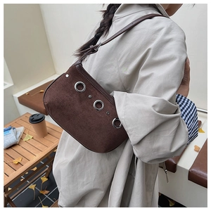 Close-up of brown suede shoulder bag with metallic silver rivets in an autumn outdoor setting