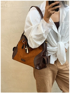 Detail of suede crossbody bag featuring a branded metal tag and decorative wooden beads