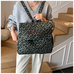 Close-up of leopard print canvas backpack with red script embroidery and brass buckles