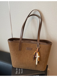 Brown suede tote bag with leather handles and colorful beaded charm on fashion books