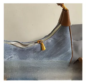 Close-up of golden hardware zipper and denim texture on the blue crescent underarm bag