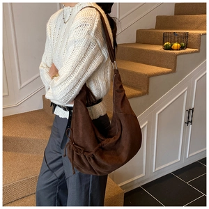 Detail of dark brown suede hobo bag with drawstring and thin strap on a model