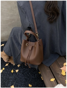 Brown litchi grain leather bucket bag featuring a drawstring closure and gold hardware details