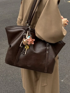 Large dark brown tote bag with metal eyelets and a bear charm on a camel coat