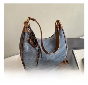 Detail of vintage denim underarm bag with brown leather trim and woven keychain charm