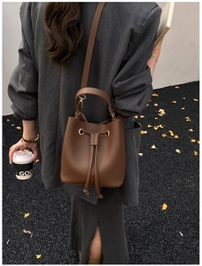 Brown lychee leather bucket bag with drawstring detail shown on a grey blazer model