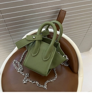 Detail of green litchi grain bucket bag with silver chain strap on a leather stool