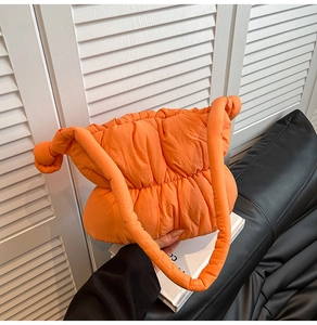 Detailed macro view of vibrant orange quilted cloud bag with padded nylon strap and texture