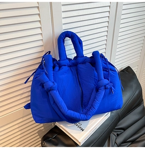 Detail of padded blue tote bag with quilted texture and knotted strap on white book
