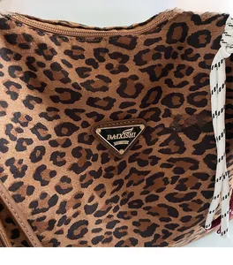 Detail of leopard print tote bag featuring a metal brand plaque and woven knotted zipper pull