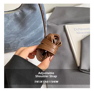 Detail view of the adjustable brown leather strap on a blue denim underarm handbag