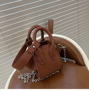 Detail of caramel leather bucket bag with silver chain on brown leather stool