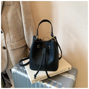 Detail of black lychee grain leather bucket bag with gold hardware and drawstring closure
