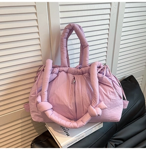 Detail of purple quilted puffer tote bag with drawstring closure on white books