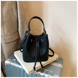 Close-up of black lychee grain leather bucket bag with gold hardware on a luxury background