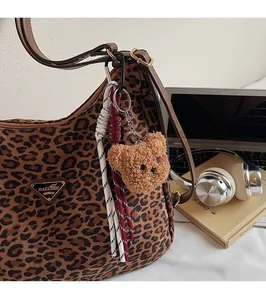 Close-up of leopard print shoulder bag featuring plush bear pendant and metal logo