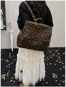 Detail view of leopard print canvas backpack with red embroidery and gold studs on flap