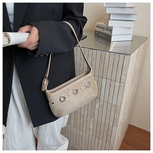 Detail of minimalist beige suede handbag with metallic eyelet accents and adjustable strap