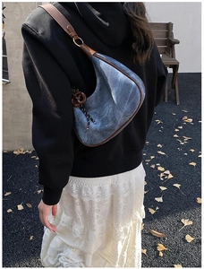 Detailed side view of denim crescent bag with brown leather trim and tassel on a model