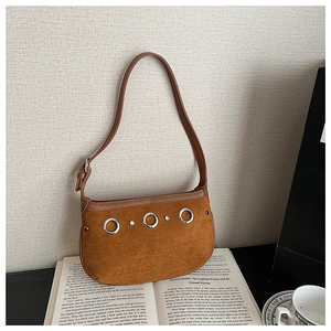Detailed macro of brown suede shoulder bag featuring silver metal rings and rivets